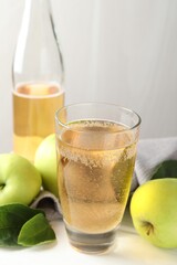 Fresh cider in glass, bottle and apples on white wooden table, closeup