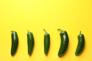 Green jalapeno peppers on yellow background, flat lay. Space for text
