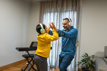 Happy father and son dancing together in their living room, enjoying music and creating joyful memories during their leisure time