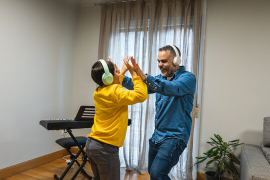 Happy father and son dancing together in their living room, enjoying music and creating joyful memories during their leisure time