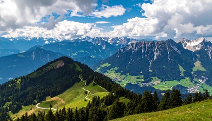 Obraz premium Panoramic vista of a mountain range with lush valleys, winding paths, and snow-capped peaks under a partly cloudy sky.