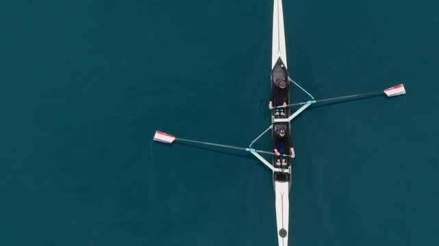 Two athletes rowing a sculling boat on calm blue water, teamwork and endurance in competitive sport. Rowers are practicing sport rowing. Rowers in a racing boat row in slow motion video 120fps.