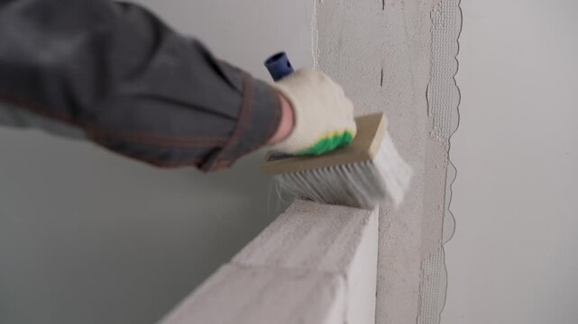 Professional builder using a large brush to apply a primer solution to an autoclaved aerated concrete block wall before plastering