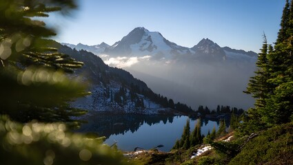 Serene mountain lake reflects jagged peaks and misty sky through evergreen trees