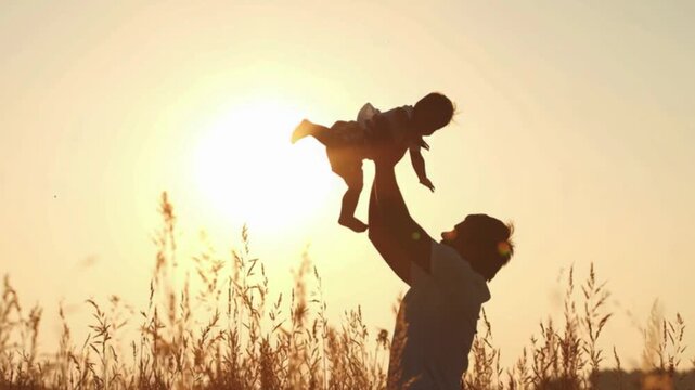 Father throws his son up in the air at sunset, silhouette of parent lifting child against golden sky, happy family bonding outdoor lifestyle, joyful fatherhood parenting love concept, cinematic video 