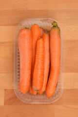 A top-down close-up view of a plastic container filled with fresh, unwashed carrots on a wooden surface