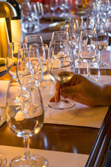 Close-up of a hand holding a glass of white wine during a wine tasting session. Transparent glass with golden liquid reflecting light, surrounded by other glasses on the table. Concept of luxury