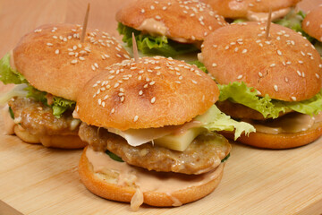 A close-up, low-angle shot of a group of homemade sesame seed burgers arranged on a rustic wooden...