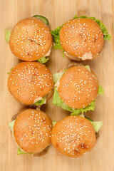 A top-down shot of six fresh, homemade sesame seed burgers arranged in two rows on a rustic wooden board