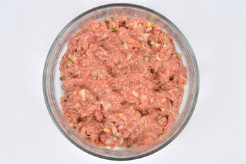 A top-down studio shot of a glass bowl containing ground pork and beef mixed with onions and spices on a white background