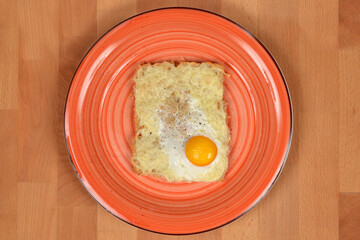 A top-down shot of a cheese and fried egg toast on a swirled orange plate on a wooden table