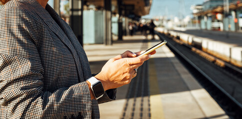 Smartphone in hands of female commuter on railroad platform station.