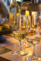 Close-up of glasses of white wine during tasting. The drink is poured from the bottle into a transparent glass, a warm golden atmosphere is created around. A stylish and atmospheric shot, perfect for