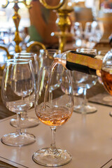 Close-up of rose wine being poured into a crystal glass during an elegant wine tasting session. The scene captures luxury, sophistication, and the art of winemaking, with soft golden reflections and a