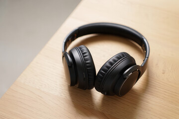 Close up shot of black wireless headphones resting on a light wooden surface in a well lit environment