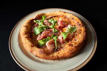 Pizza with Arugula and Ham: An overhead shot of a freshly baked pizza topped with savory ham, peppery arugula, all nestled on a rustic plate.