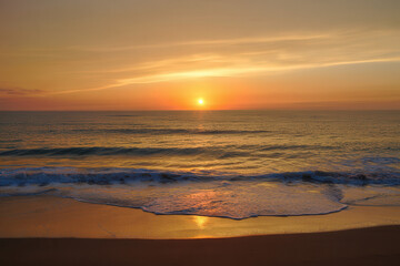 Naklejka premium Golden sunset reflecting on the ocean waves washing up on the sandy beach shore line view