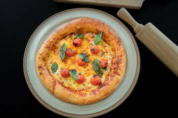 Gourmet Pizza Delight: Savor a delicious gourmet pizza, freshly baked and adorned with vibrant cherry tomatoes and fragrant basil leaves on a plate, with a rolling pin.
