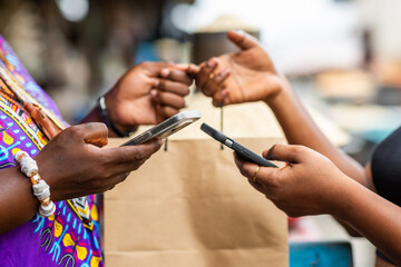 Smartphones contactless payment at local traditional African market. Mobile money transactions at outdoor stall.