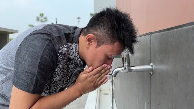 Muslim man washing face with clean water from faucet during ablution ritual before Islamic prayer