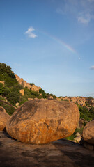 A view of Hampi's golden boulders with a rainbow and the moon at sunset.