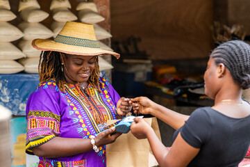Contactless payment in Africa. A customer makes a successful transaction via mobile point of sale, POS terminal at an outdoor local traditional market.