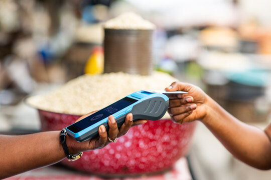 Contactless payment with a credit card at an outdoor African grains local traditional market with a handheld point of sale, POS terminal.