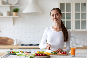 Woman in her kitchen is cutting vegetables to prepare healthy food, following proper nutrition principles