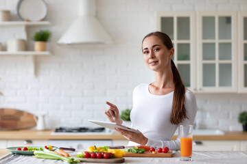 Woman in the kitchen with electronic tablet preparing fresh vegetables