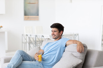 Handsome young man sitting on the sofa in the living room with juice, relaxing