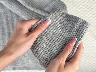 Obraz premium A woman holds the sleeve of a warm gray sweater with bobbles, checking fabric pilling. Preparing and caring for clothes, wardrobe organization for autumn and winter fashion seasons