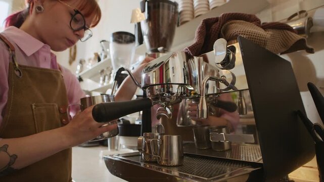 Low angle view of young tattooed barista in apron steaming milk in pitcher while preparing coffee in cafe