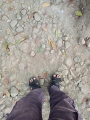Feet in sandals standing on a path with rocks