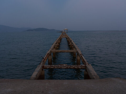 abandoned pier extending into calm sea under dusk sky with distant islands and tranquil atmosphere