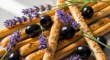 Close-up of crispy breadsticks seasoned with salt and herbs, adorned with black olives and fragrant lavender sprigs.