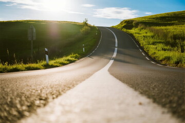 Sunlit winding road through green rolling hills under clear sky