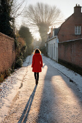 figure draped in striking red coat walks down narrow wintery alley illuminated by soft glow of setting sun