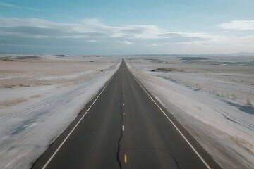 Long straight road stretching through a snowy open landscape under a clear sky