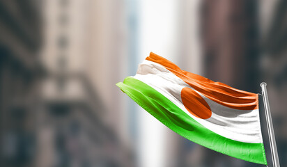 Niger national flag waving on street. A beautiful with mast with blur buildings. Niger national flag for independence day.