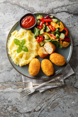 Close-up of Spanish chicken croquettes with mashed potatoes, vegetable salad, and ketchup in a plate on a table. Vertical top view from above