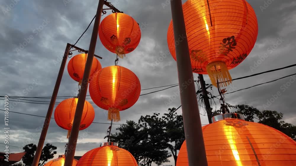 Poster a bunch of orange lanterns are hanging from a wire, with each one lit up. the lanterns are arranged 