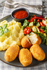 Chicken Croquettes Croquetas de Pollo with mashed potatoes, vegetable salad and ketchup close-up in a plate on the table. Vertical