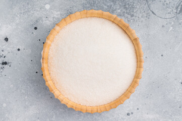 Versatile white sugar in a rustic bowl, ready to enhance desserts and beverages with its delightful sweetness. grey background. top view