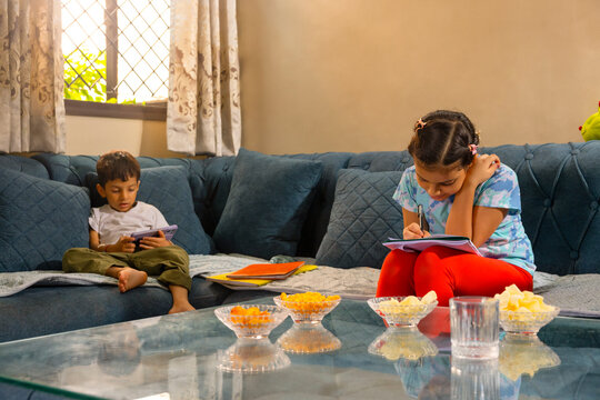 Brother and sister spending quiet time together, one using a phone while the other studies with a notebook