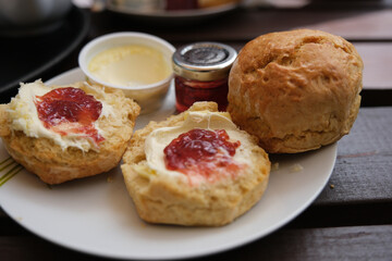 Freshly baked scones served with clotted cream and strawberry jam on wooden table.