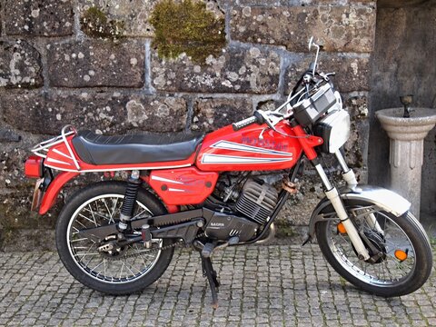 Red mobylette motorcycle parked near stone wall in Portugal