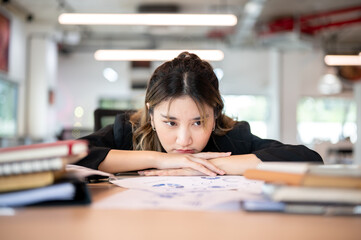 Annoyed asian businesswoman resting head on folding arms at working table or desk in the office.