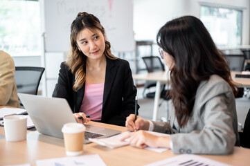 Asian businesswoman looking at a coworker during a planning while sitting at wooden table in office.