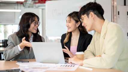 Smiling asian businesswoman and coworkers talking in front of a laptop while making a plan in office