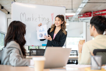 Naklejka premium Asian businesswoman holding document explaining marketing plan on whiteboard to coworkers in office.